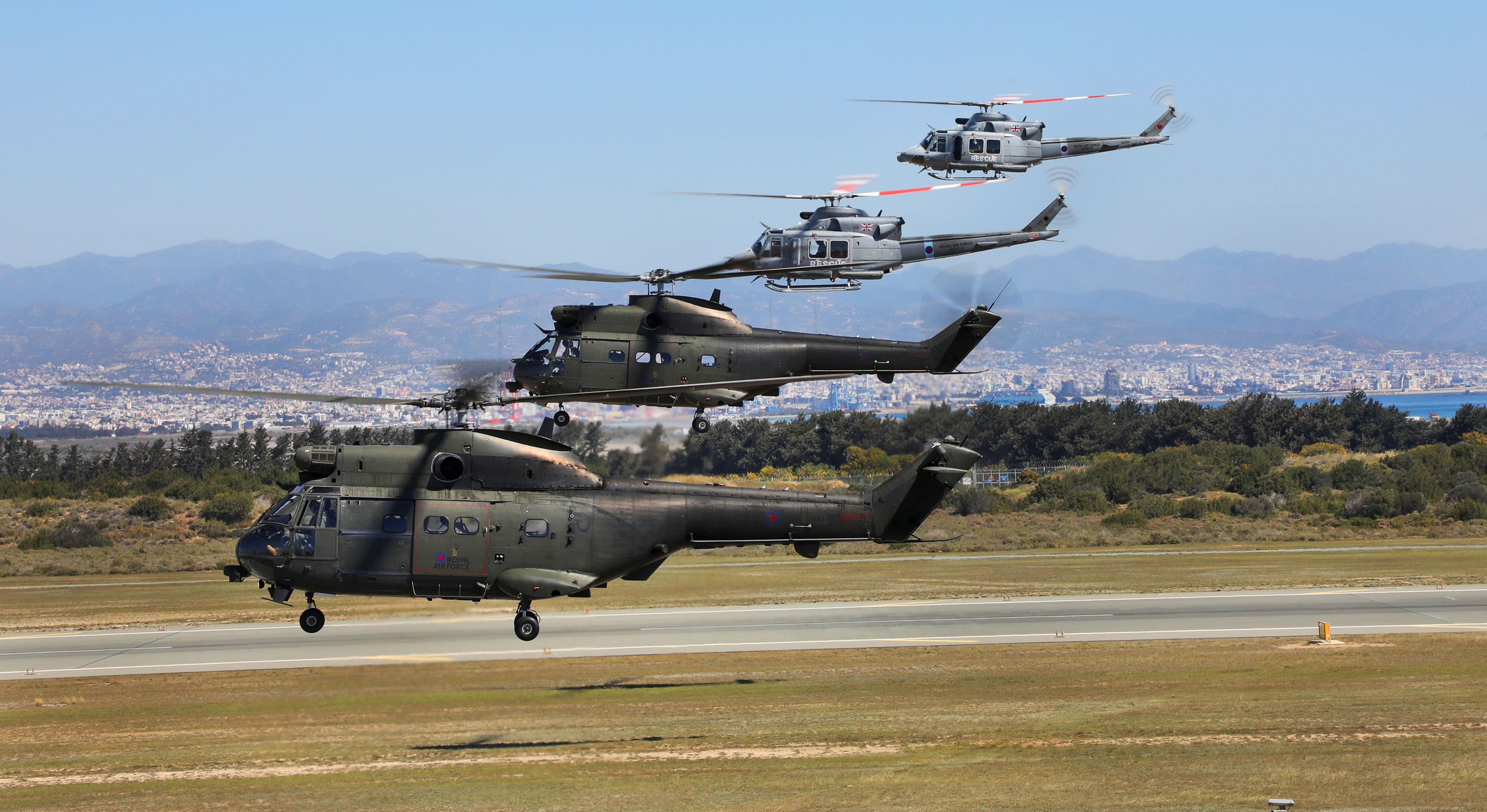 Image shows RAF Puma and Griffin helicopters in flight over the airfield runway.